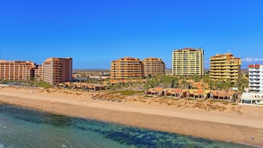 Una zona turística a la costa amb diversos edificis alts, una platja sorrenca i aigües blaves i cristal·lines.