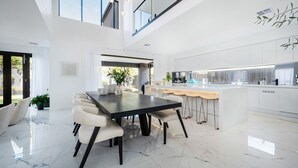A modern kitchen with white cabinetry, a marble countertop, and a central island with bar stools. - Villa Capri | Luxe Modern by the Village (Mount Eliza)