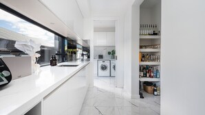 A modern kitchen with a long countertop, built-in appliances, and a wine rack. - Villa Capri | Luxe Modern by the Village (Mount Eliza)