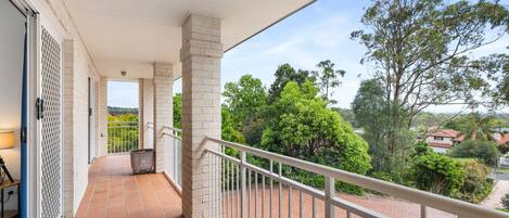 A balcony with a tiled floor, white railings, and a view of trees and houses.