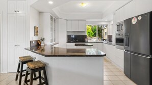 A modern kitchen with white cabinets, a black refrigerator, and a central island with stools. - Peaceful Family Home: 4-bed, Pool, Alfresco Dining (Brisbane)