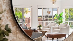 A modern living room with a large mirror reflecting the space, featuring a sofa, armchairs, a coffee table, and a chandelier. - Peaceful Family Home: 4-bed, Pool, Alfresco Dining (Brisbane)