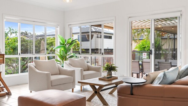 A spacious living area with large windows, a coffee table, sofas, and a view of the outdoors. - Peaceful Family Home: 4-bed, Pool, Alfresco Dining (Brisbane)