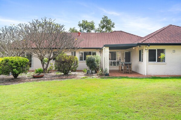 A two-story house with a covered patio and a small garden. - Peaceful Family Home: 4-bed, Pool, Alfresco Dining (Brisbane)