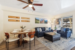 A modern living room with a dining area, a ceiling fan, and wall art.