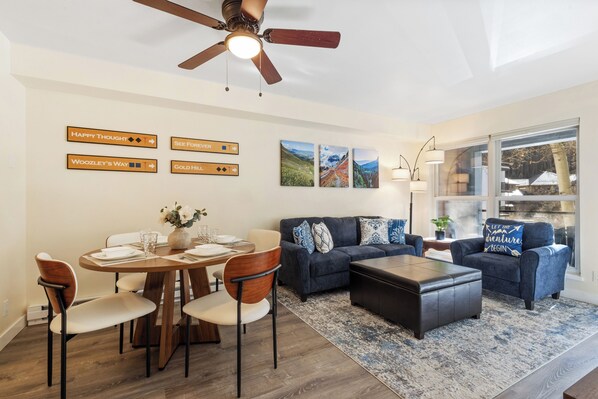 A modern living room with a dining area, a ceiling fan, and wall art.
