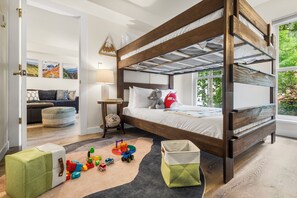 A bunk bed with a wooden frame, a bedside table with a lamp, and a window with a view of greenery.