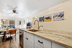 Una cocina con encimera de granito, lavavajillas y comedor con sillas y mesa.