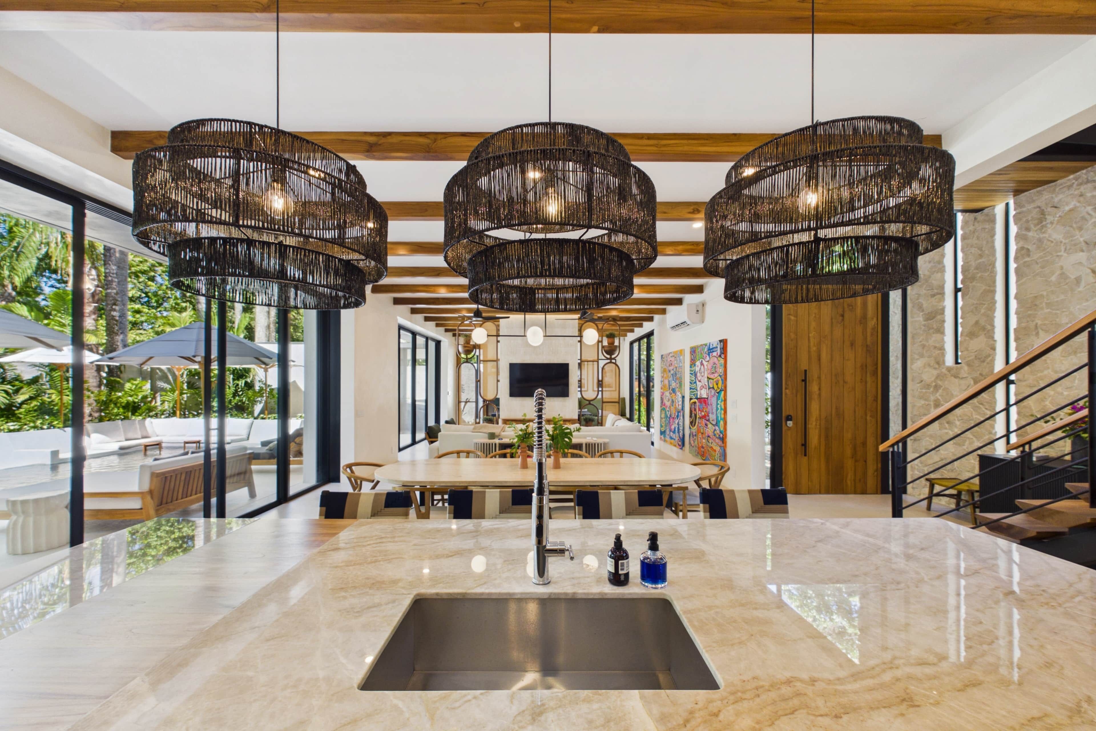 A modern kitchen with a marble countertop, a stainless steel sink, and three hanging pendant lights.