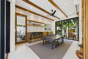 A modern indoor space with a ping pong table, wooden chairs, and a ceiling fan.