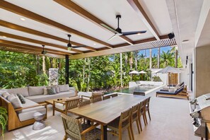A modern outdoor dining area with a wooden table and chairs, a sofa, and a poolside lounge.