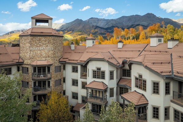 A multi-story building with a stone facade, multiple balconies, and a mountainous backdrop.