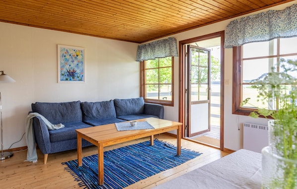 Un salon chaleureux avec un canapé bleu, une table basse en bois et un tapis bleu. Un tableau orne le mur, et une fenêtre est agrémentée d’une lambrequin à motifs.