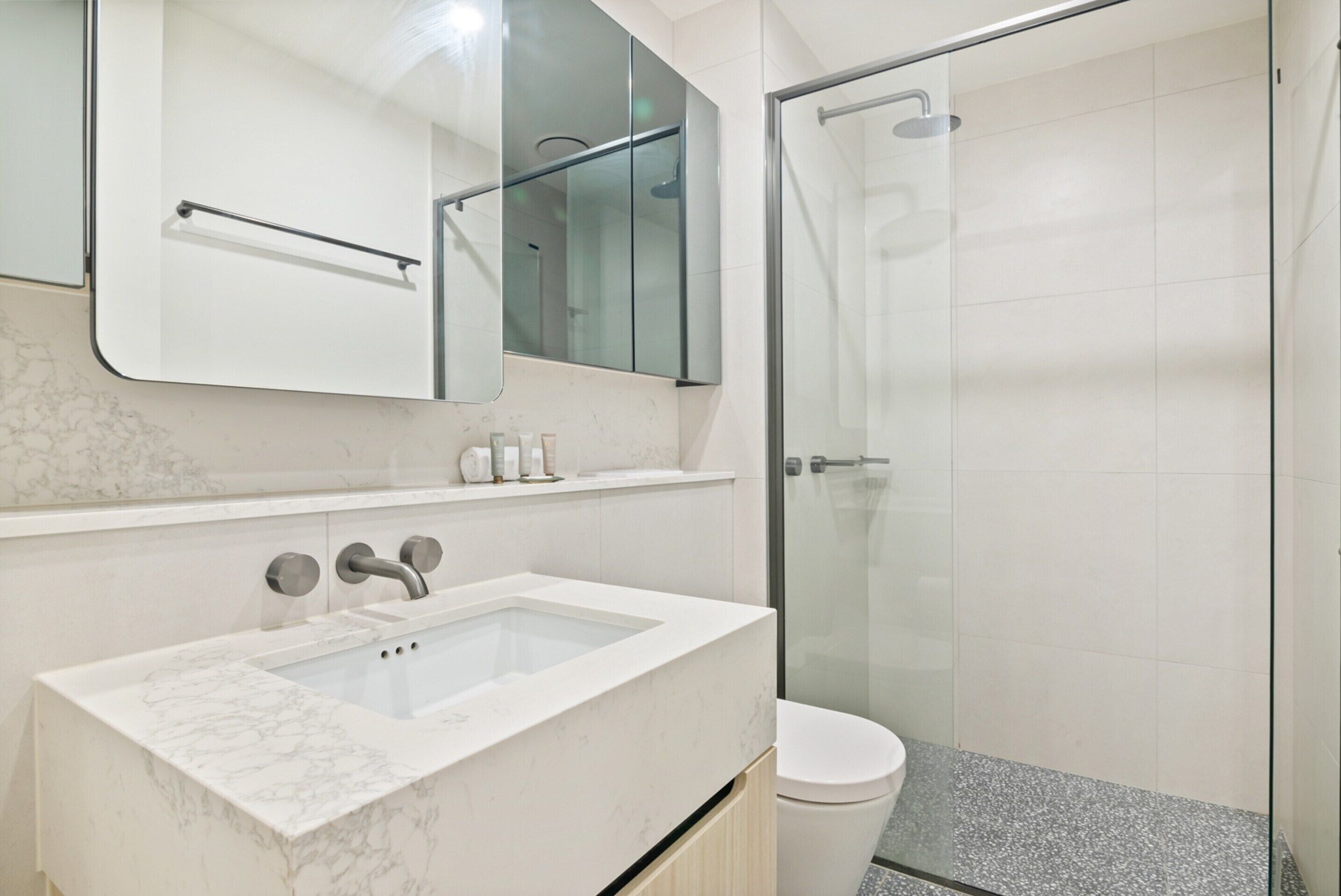 A modern bathroom with a marble sink, a glass shower enclosure, and a toilet.