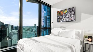 Un dormitorio moderno con una cama grande, vistas de la ciudad a través de ventanales y un cuadro en la pared.