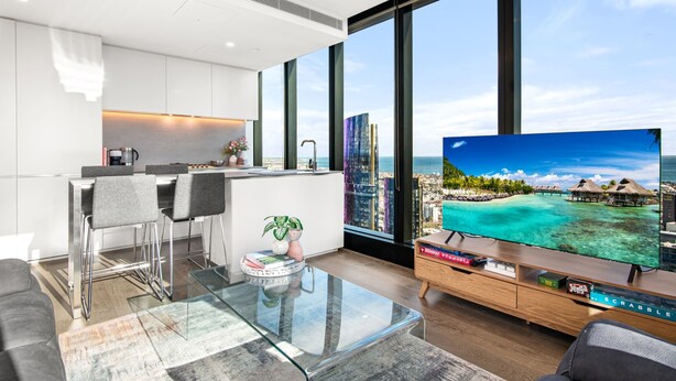 Una sala moderna con una mesa de centro de vidrio, un sofá y un televisor que muestra una escena tropical.