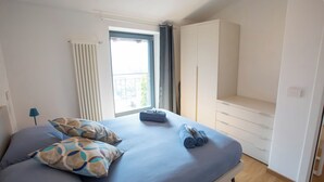 A bedroom with a bed, pillows, a window with curtains, a radiator, and a wardrobe. - Apartment on the Sentiero Valtellina bike path, just minutes from Lake Como (Morbegno)