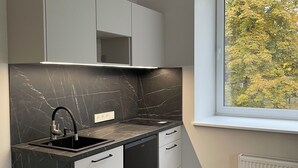Een moderne keuken met zwarte marmeren aanrechtbladen, witte kasten en een raam met uitzicht op bomen.