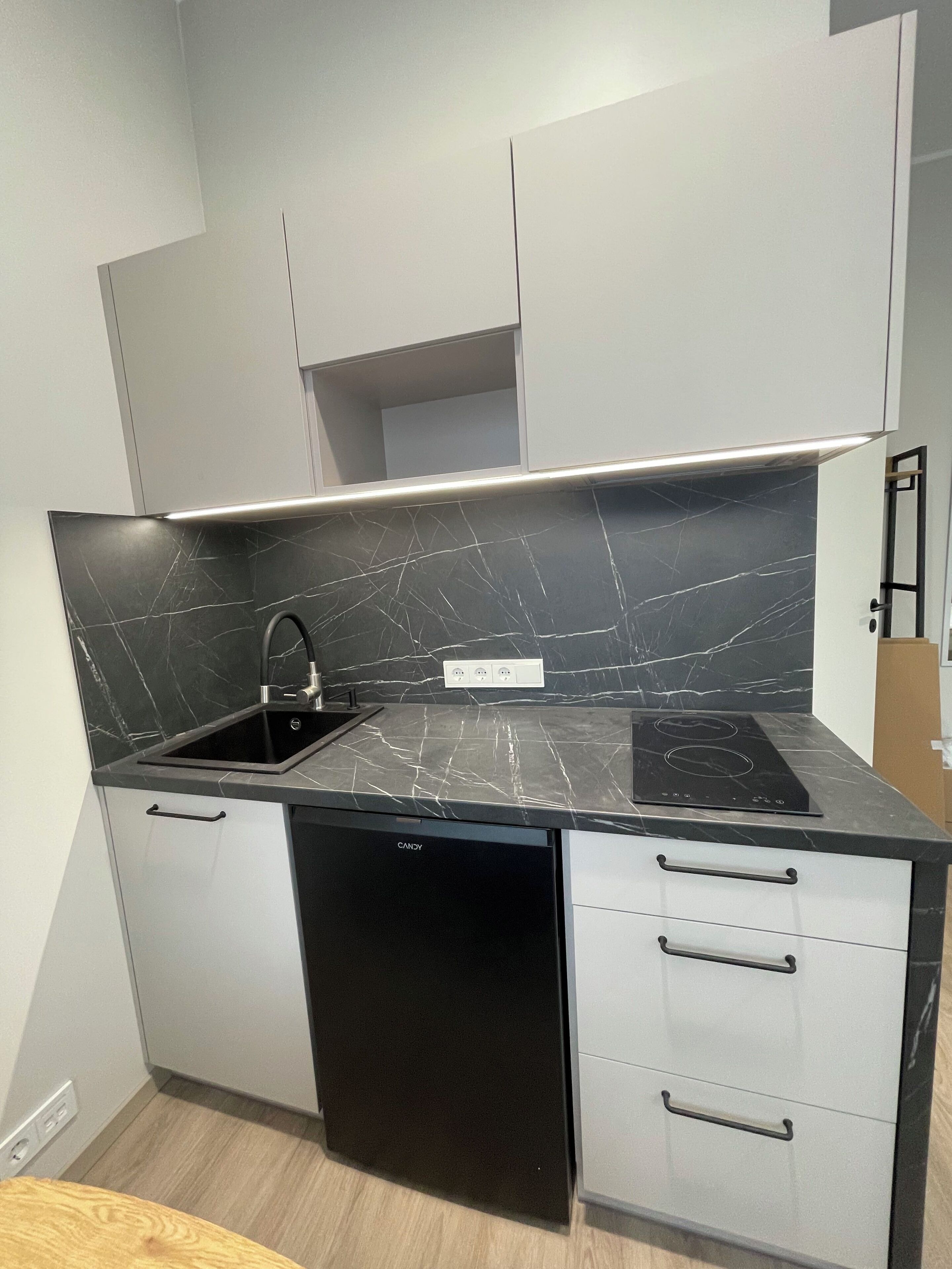 A compact kitchen with a black countertop, white cabinets, and a built-in dishwasher.