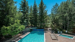 Une piscine rectangulaire bordée d’une terrasse en briques, entourée d’arbres et agrémentée d’une petite cascade.