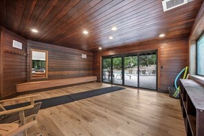 Une pièce spacieuse dotée d’un plancher en bois, d’un banc, d’un grand miroir et d’une porte-fenêtre coulissante donnant sur un espace extérieur aménagé avec des chaises et une piscine.