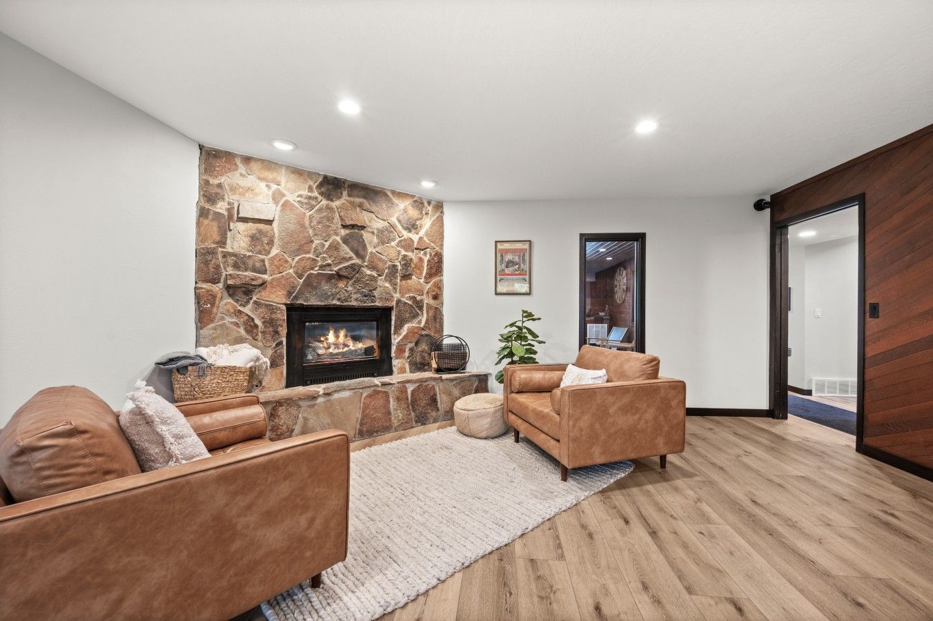 Una sala de estar moderna con chimenea de piedra, sofás de cuero y suelo de madera.