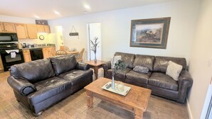 Un salon avec un canapé en cuir marron, une table basse en bois et un coin repas comprenant des chaises et une table en bois.