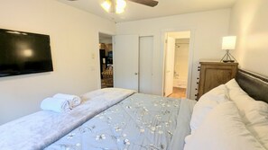 Une chambre à coucher comprenant un lit, un téléviseur fixé au mur, une armoire en bois et une porte donnant sur une salle de bain.