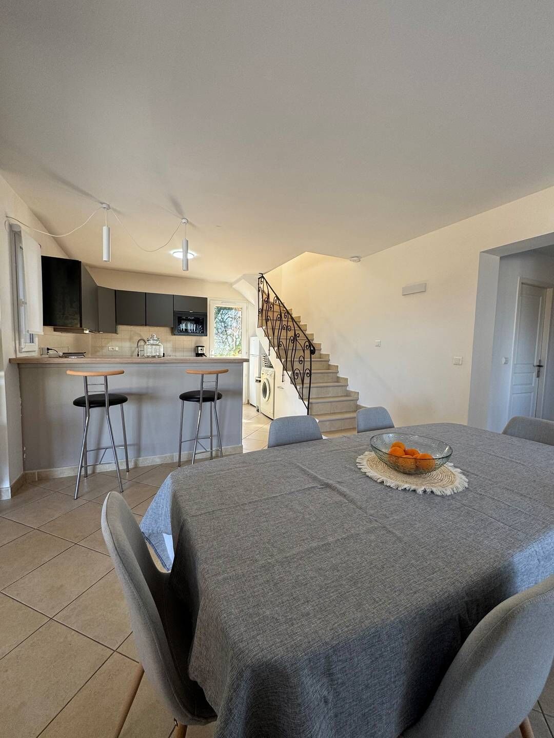 A modern kitchen with a central island, a dining area with a table set for two, and a staircase leading to an upper level.