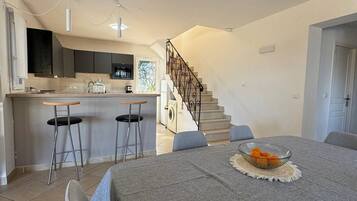 A modern kitchen with a central island, a dining area with a table set for two, and a staircase leading to an upper level.