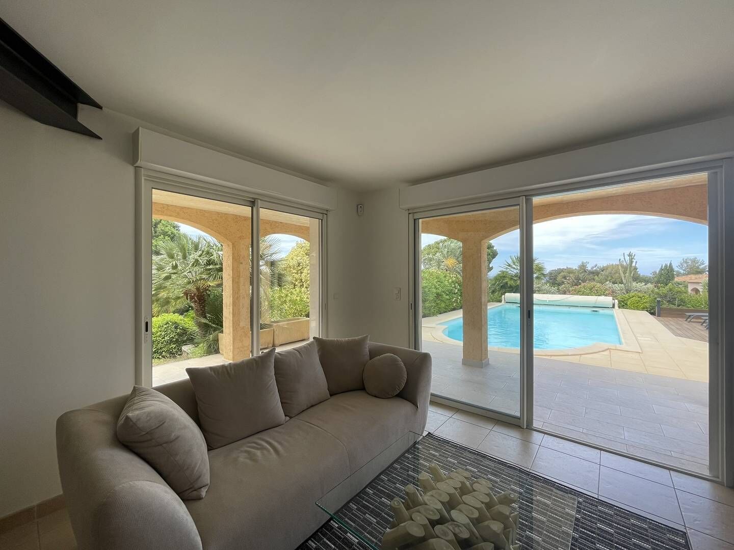 A modern living room with a beige sofa, large sliding glass doors leading to a pool area.