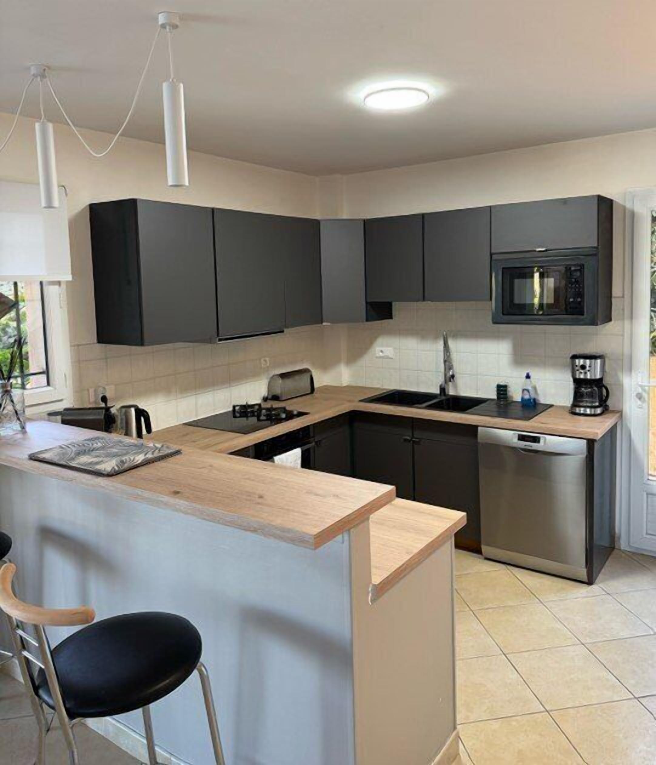 A modern kitchen with a central island, dark cabinets, a microwave, and a dishwasher.