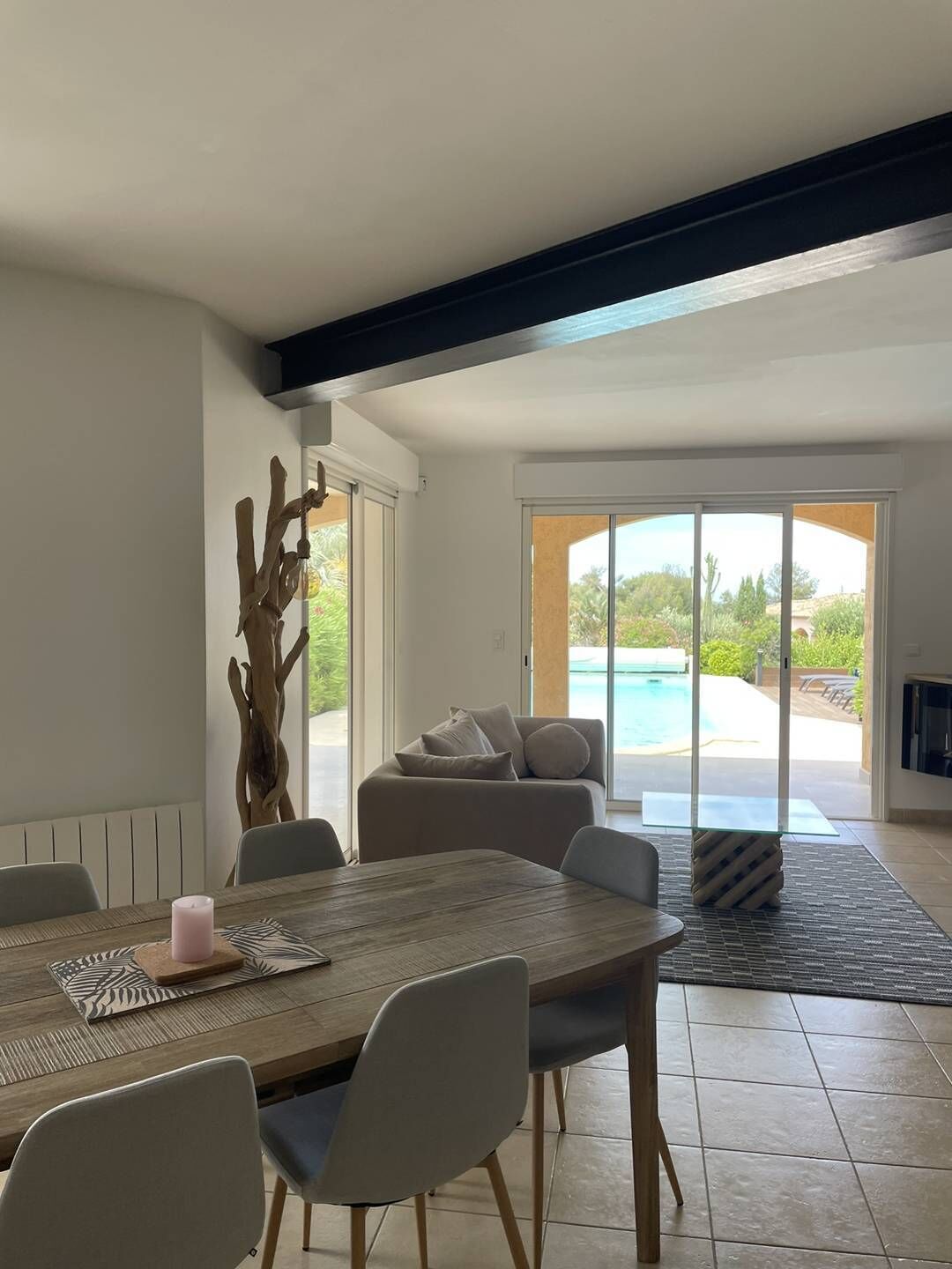 A modern living room with a dining area, a large window, and a view of a swimming pool.