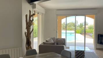 A modern living room with a dining area, a large window, and a view of a swimming pool.