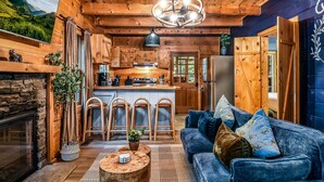 L’intérieur chaleureux d’un chalet avec un plafond en bois, une cheminée, un canapé bleu et un coin cuisine.