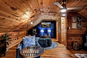 A cozy room with wooden walls and ceiling, a sofa, a round coffee table with chess pieces, and a ceiling fan.