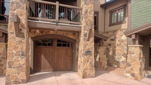 Un bâtiment en pierre avec une porte de garage en bois, un balcon et une fenêtre verte.