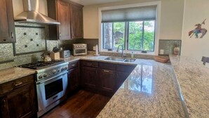 Une cuisine dotée de plans de travail en granit, d’une cuisinière, d’un four et d’une fenêtre donnant sur un paysage verdoyant.