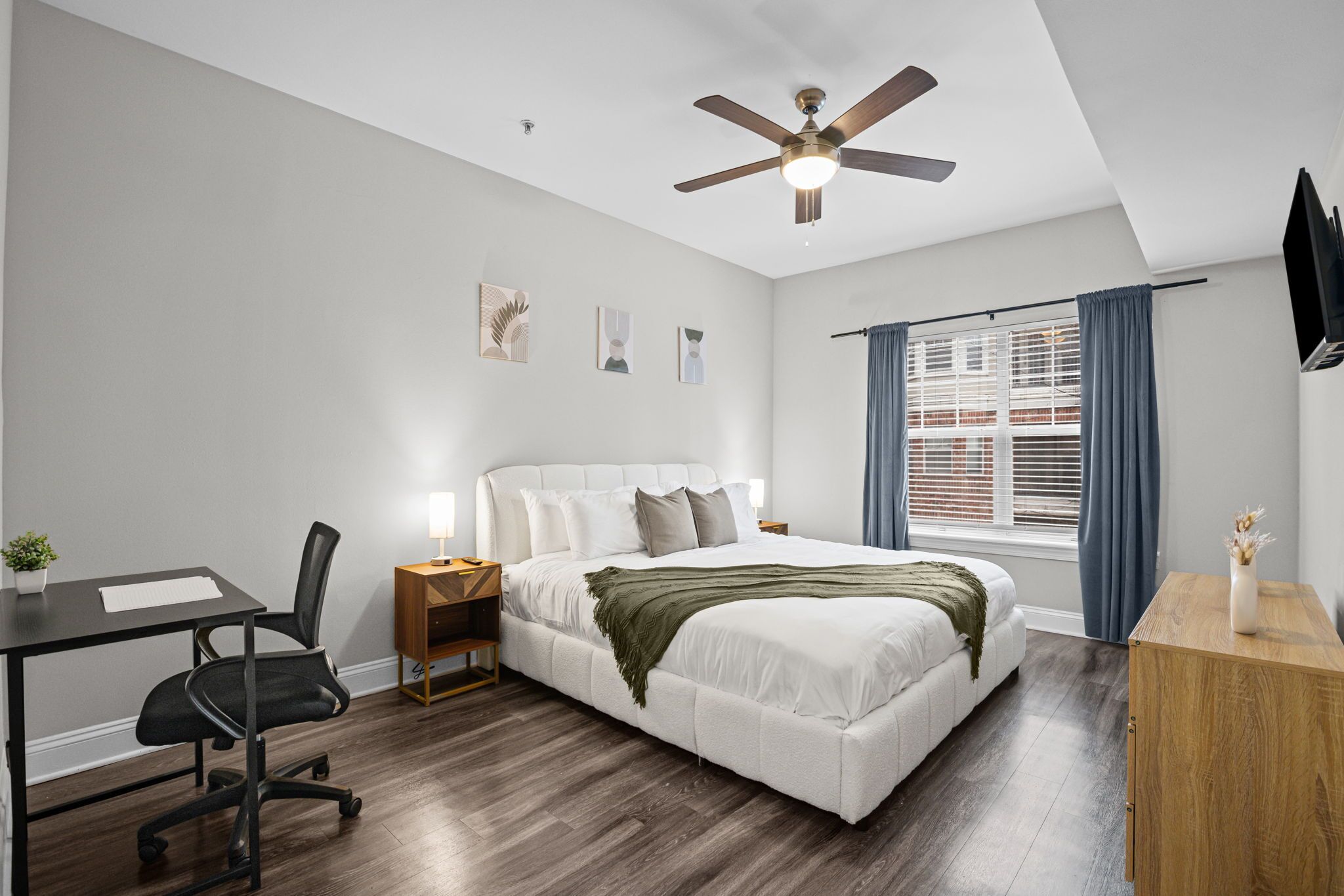A modern bedroom with a bed, desk, chair, and a ceiling fan.
