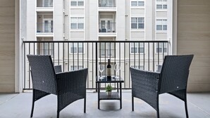 A balcony with two black wicker chairs, a small table with a bottle and glasses, and a potted plant. - High-Rise with Rooftop Pool | Gym | Balcony & Skyline Views (Atlanta)
