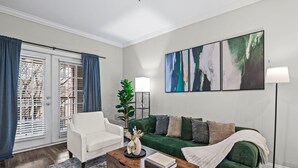 A living room with a white armchair, green sofa, and a coffee table with a book and vase. - High-Rise with Rooftop Pool | Gym | Balcony & Skyline Views (Atlanta)