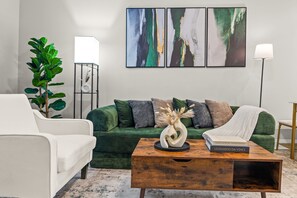 A modern living room with a green sofa, white armchair, and a wooden coffee table with books.