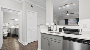 A modern kitchen with white cabinetry, stainless steel appliances, and a large mirror above the countertop. - High-Rise with Rooftop Pool | Gym | Balcony & Skyline Views (Atlanta)