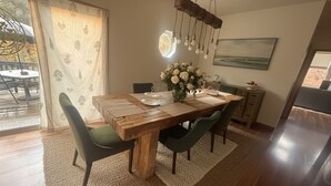 A dining area with a wooden table, green upholstered chairs, a vase with white flowers, and a hanging light fixture.