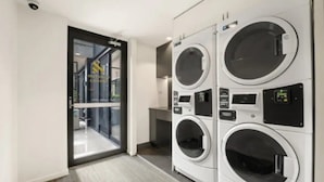 A modern laundry room with four stacked front-loading washing machines and a glass door leading to a hallway.