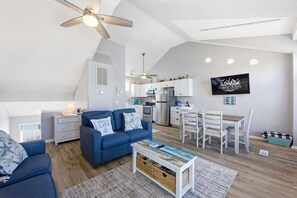 A modern apartment with a living room, kitchen, dining area, and a ceiling fan. - Salty Blue Hen: Oceanside, Community Pool, Close to Beach Access (Corolla)