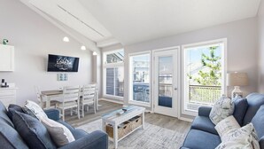 A modern living room with a sofa set, a coffee table, a TV, and a dining area with a table and chairs. - Salty Blue Hen: Oceanside, Community Pool, Close to Beach Access (Corolla)