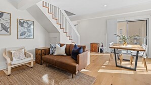 Una sala de estar moderna con un sofá marrón, una mesa de comedor de madera y una escalera con barandillas de madera.
