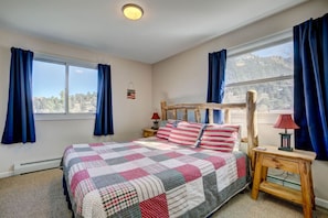 Ein Schlafzimmer mit einem großen Bett, zwei Nachttischen, einem Holzkopfende und Blick ins Freie.