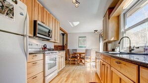 A modern kitchen with wooden cabinets, a built-in oven, and a microwave. There is a dining area with a table and chairs. - Lakeshore Retreat- Estes Park Escape with Mountain & Pond Views (Estes Park)